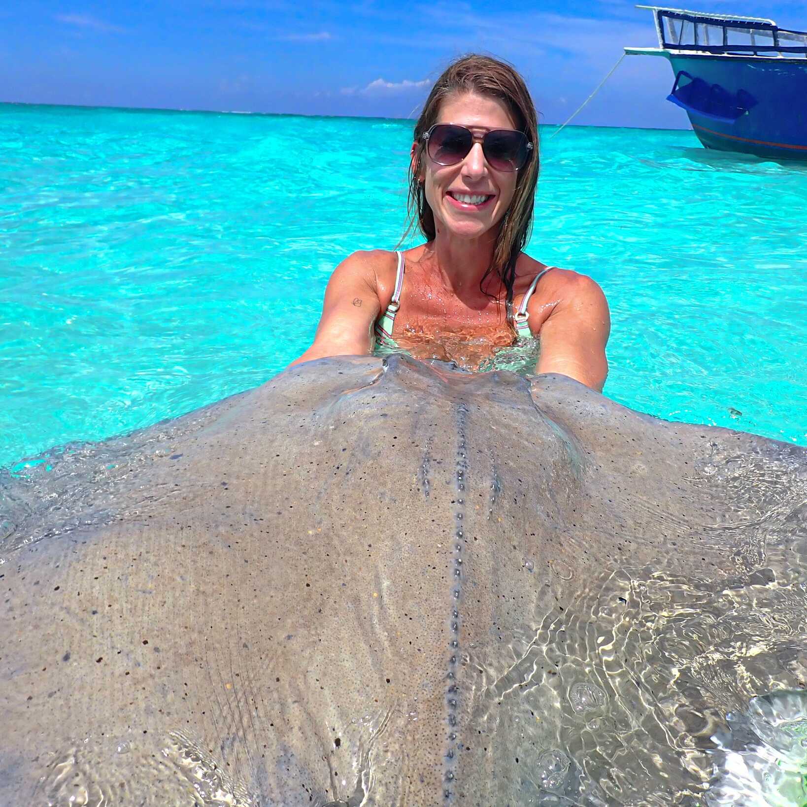 Sequel travel advisor Deana bathing in clear turquoise ocean water while holding a manta ray