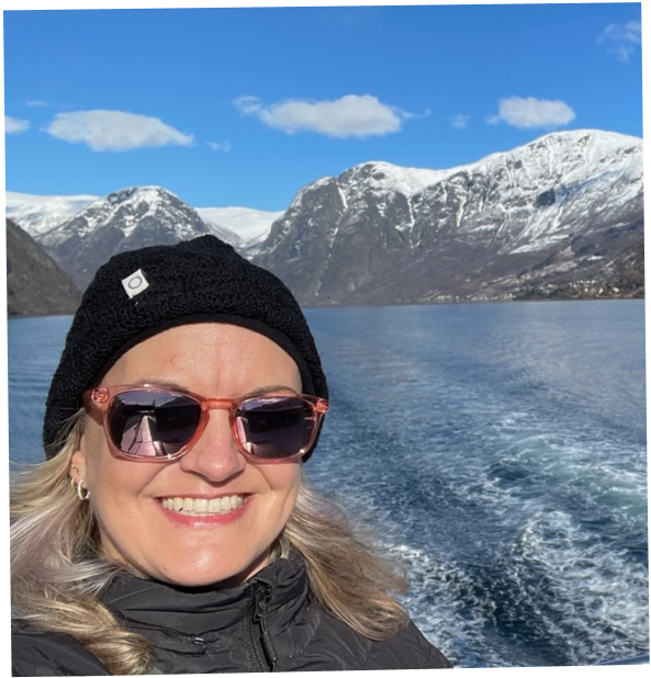 Travel advisor, Lisa, taking a selfie off of the back of a boat with the stunning snowcapped mountains of Norway in the background