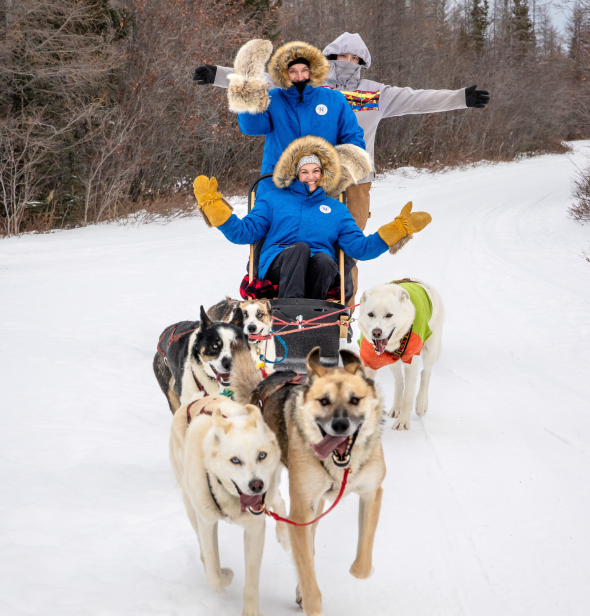 Travel agent Lisa on a vacation travel adventure is riding on a sled pulled by five dogs through the snow