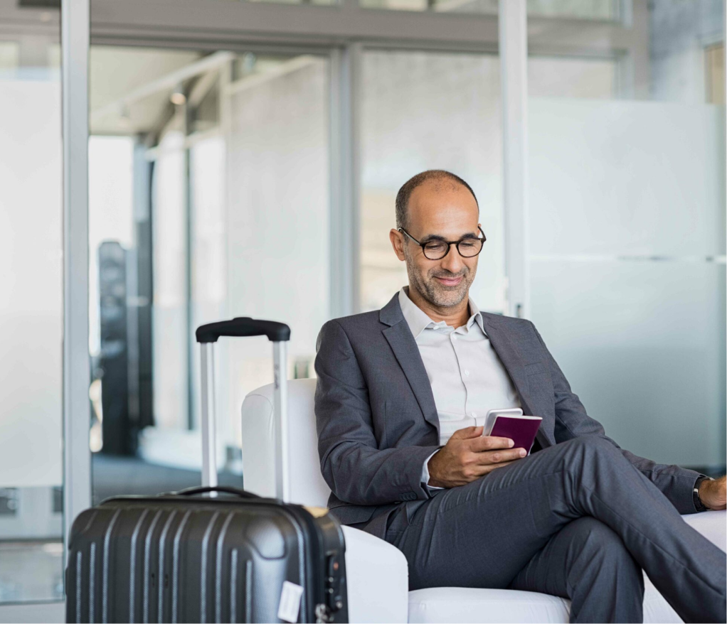 Man sitting in an airport lounge with his travel documents, looking calm and relaxed thanks to his corporate travel agent's planned itinerary