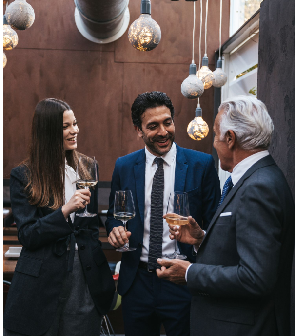 Three professionals of different ages mingling with cocktails at a networking event