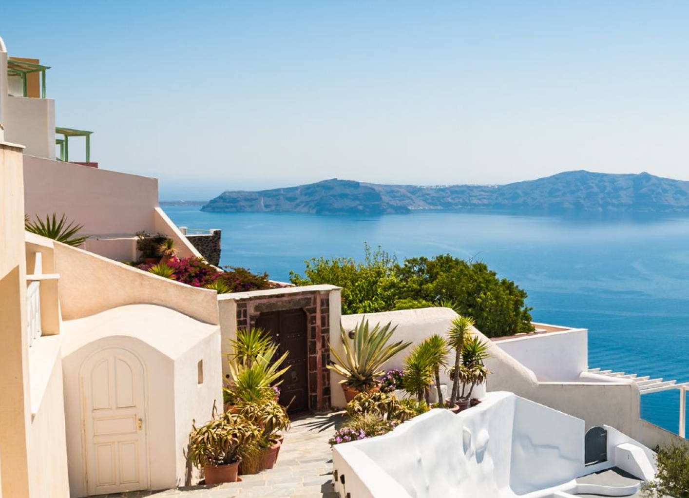 Vacation destination featuring white buildings in Greece overlooking the blue ocean, promoted by a travel agency